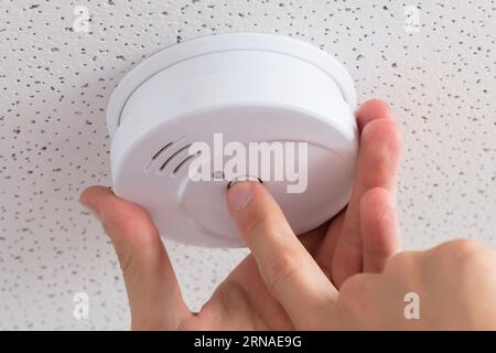 Low Angle View Of A Person's Hand Installing Smoke Detector On Ceiling Wall At Home Stock Photo
