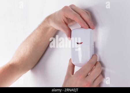Close-up Of Young Male Electrician Installing Security System Door Sensor On Wall Stock Photo