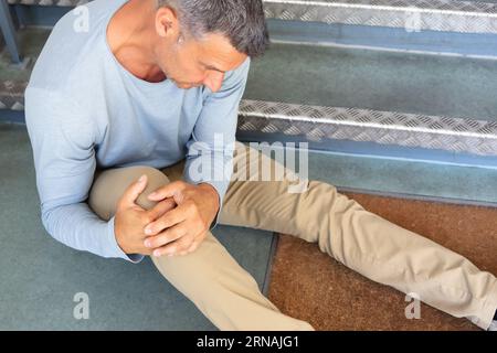 Mature Man Sitting On Staircase After Slip And Fall Accident Stock Photo