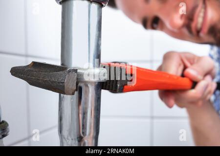 Young Male Plumber Repairing Sink With Adjustable Wrench In Bathroom Stock Photo