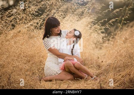 mother and daughter sitting on ground in field in afternoon Stock Photo