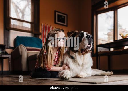 Little girl sits on floor in living area with St. Bernard dog Stock Photo