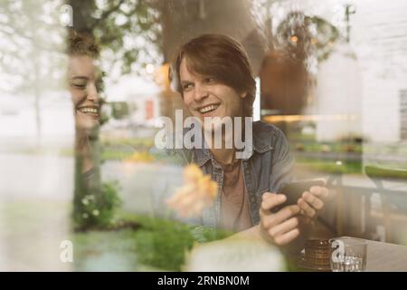 Cheerful young couple sitting with smartphone at table Stock Photo