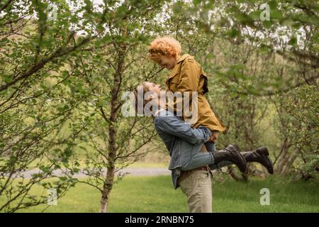 Happy man lifting girlfriend in park on sunny day Stock Photo