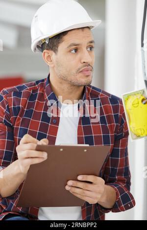 smiling handsome electrician holding clipboard near electrical box Stock Photo