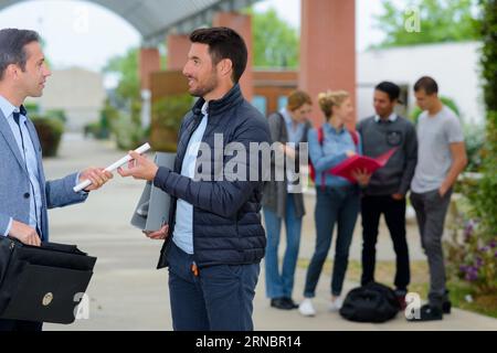two adult men on campus passing papers Stock Photo