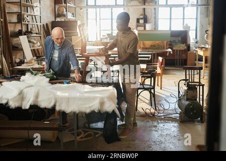 Full length portrait of two workers refurbishing vintage furniture in rustic workshop, copy space Stock Photo