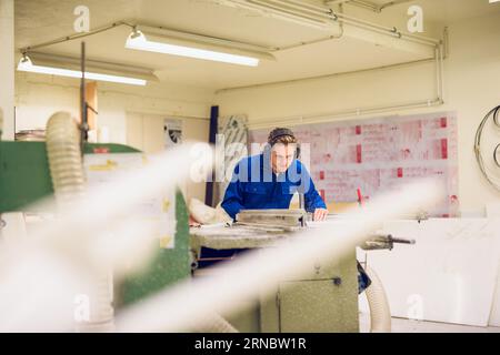 Focused young craftsman working in factory with earmuffs Stock Photo