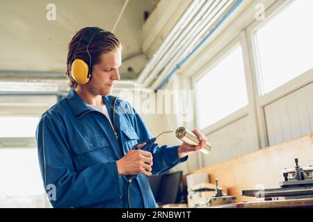 Focused young man in earmuffs standing with tools in factory Stock Photo