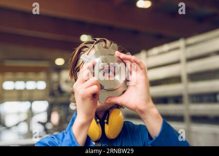 Unrecognizable man with earmuffs and machine part in hands Stock Photo