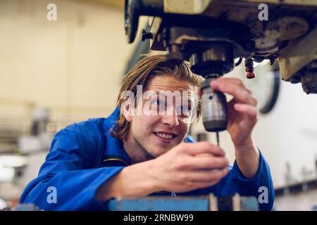 Happy young man standing at drilling machine and repairing in factory Stock Photo