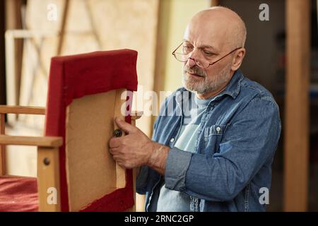 Portrait of experienced senior craftsman restoring old furniture items in workshop Stock Photo
