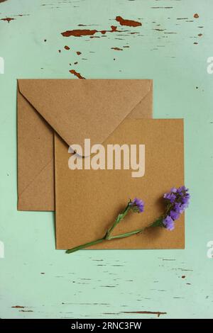 an empty  brown card with a purple blooming flower on top on a mint background with paint peeling off Stock Photo