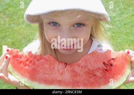 Happy little girl with big watermelon slice. Cild eating fruit. Outdoor close up portrait. Stock Photo