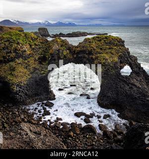 Lichen and moss covered stone bridge at Arnarstapi, Snaefellsness Peninsula, Iceland. The sea arch is known as Gatklettur, or the Hellnar Arch. Stock Photo