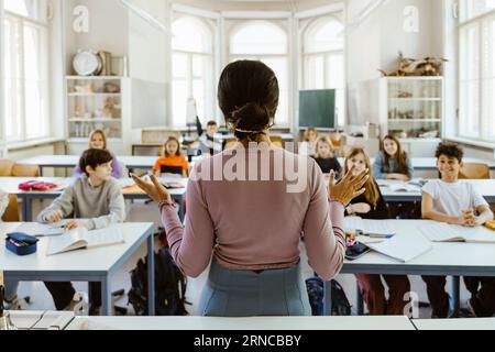 Rear view of female teacher explaining students sitting in classroom Stock Photo