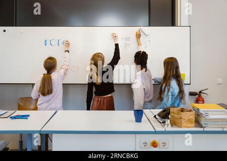 Female students writing on whiteboard in classroom Stock Photo