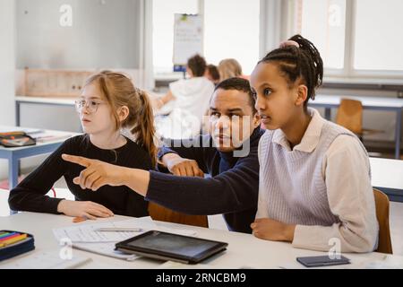 Male teacher pointing by female students sitting at desk in classroom Stock Photo