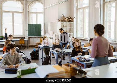 Male and female students listening to teacher teaching in classroom Stock Photo