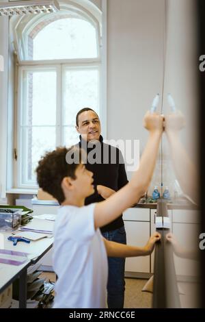 Male teacher looking at student writing on whiteboard in classroom Stock Photo