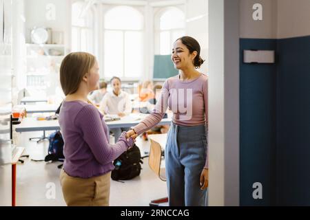 Smiling female teacher doing handshake with student standing in classroom Stock Photo