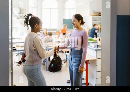 Schoolgirl doing handshake with female teacher standing in classroom Stock Photo