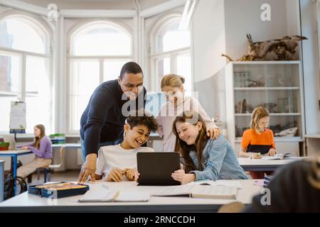 Happy male and female students enjoying while watching tablet PC with teacher in classroom Stock Photo