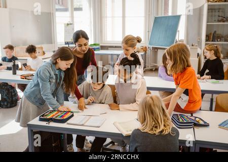 Female teacher assisting students learning together in classroom Stock Photo