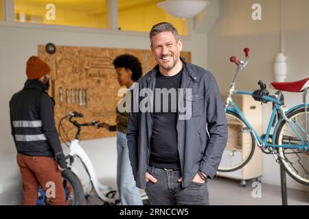 Portrait of happy man with hands in pockets during cycle repairing workshop at recycling center Stock Photo