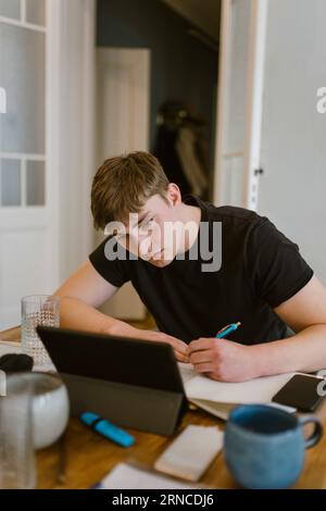 Young man writing while studying from digital tablet at home Stock Photo