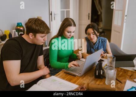 Young friends using laptop while doing school assignment together at home Stock Photo