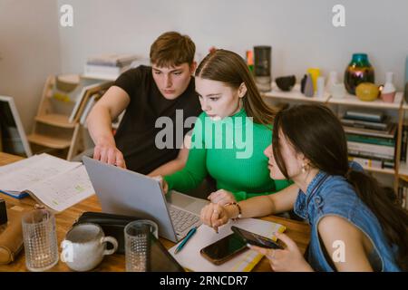 Young friends doing school assignment together while using laptop at home Stock Photo