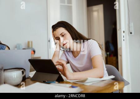 Bored young woman using digital tablet while studying at table Stock Photo