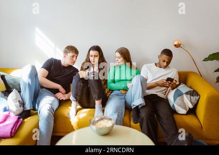 Young multiracial friends using smart phones while sitting together on sofa at home Stock Photo