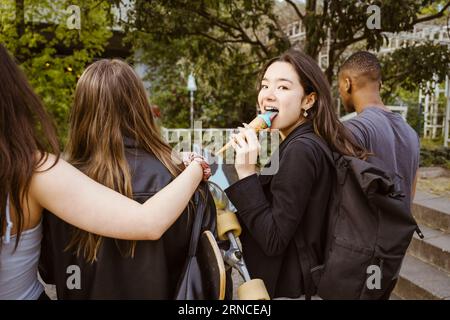 Young woman looking back while eating ice cream and walking with friends in city Stock Photo