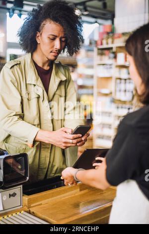 Young male customer scanning through smart phone while paying at checkout counter in store Stock Photo