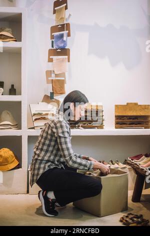 Full length side view of saleswoman crouching by box at boutique Stock Photo