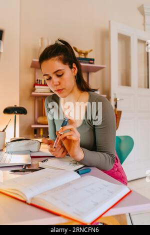 Young woman using glucometer while doing homework at table Stock Photo