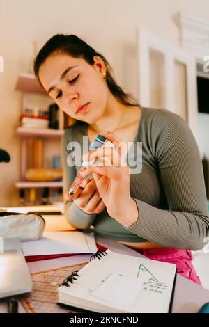 Young woman using glucometer while doing homework at home Stock Photo