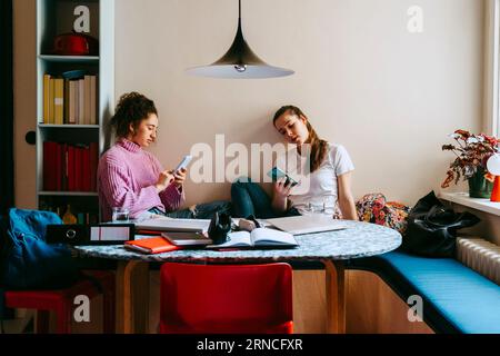 Young women using smart phones while sitting with books at home Stock Photo