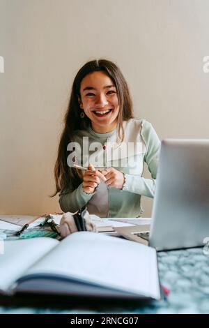 Portrait of cheerful young woman doing homework at table Stock Photo