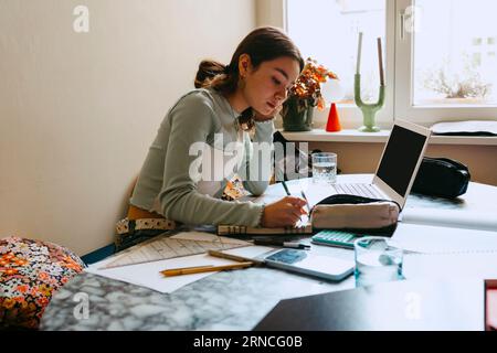 Young woman doing homework while writing in book at home Stock Photo