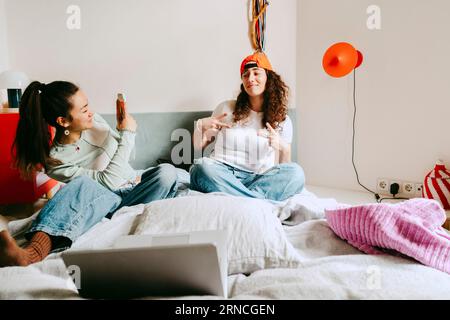 Young woman photographing female friend through smart phone at home Stock Photo