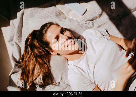 Portrait of smiling young woman lying on bed at home Stock Photo