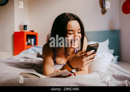 Happy young woman using smart phone while lying on bed at home Stock Photo