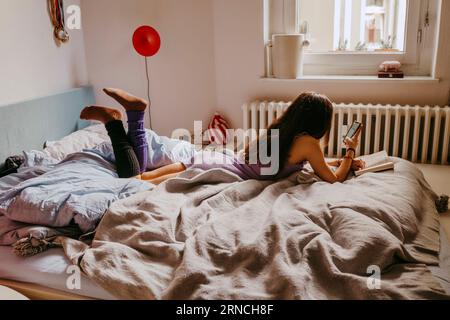 Young woman using mobile phone while lying on bed at home Stock Photo