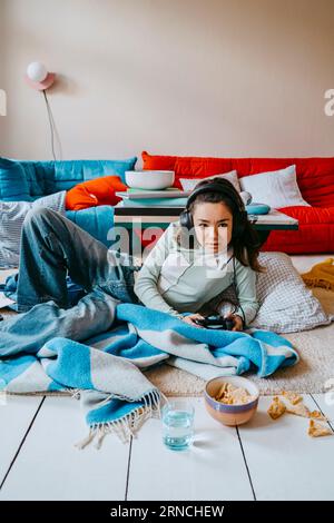 Young woman playing video game while lying in living room at home Stock Photo
