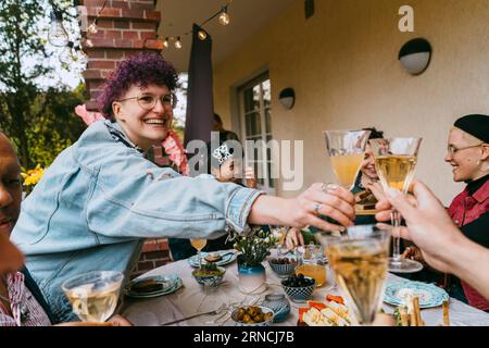 Happy non-binary person toasting drinks with friends during party in back yard Stock Photo