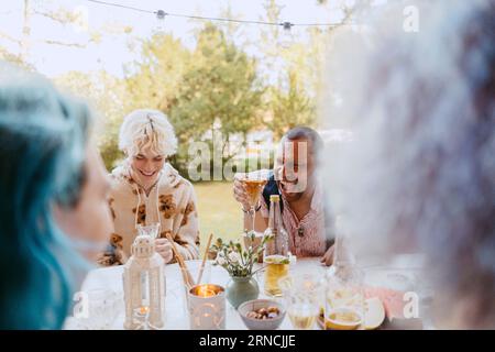 Happy gay friends laughing while having drinks with friends during dinner party in back yard Stock Photo