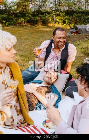 Happy gay man enjoying drinks with LGBTQ friends in back yard Stock Photo